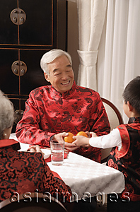 Asia Images Group - Boy presenting two mandarin oranges to grandfather at dinner table