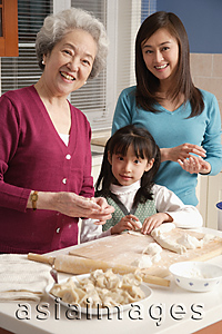 Asia Images Group - Grandmother, daughter and granddaughter making dumplings in the kitchen, looking at camera