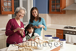 Asia Images Group - Grandmother, daughter and granddaughter making dumplings in the kitchen, looking at camera