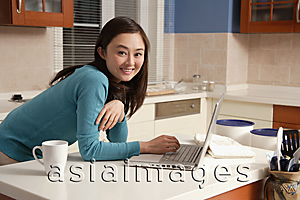 Asia Images Group - Young woman using laptop on kitchen top, looking at camera