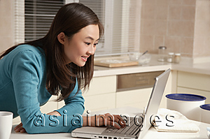 Asia Images Group - Young woman using laptop on kitchen top