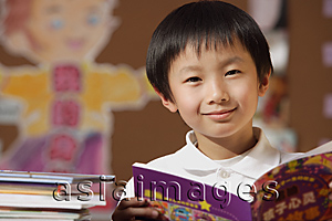 Asia Images Group - Schoolboy with book in hand in class looking at camera