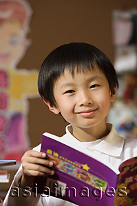 Asia Images Group - Schoolboy with book in hand in class looking at camera