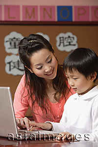 Asia Images Group - Teacher helping student use a laptop in class