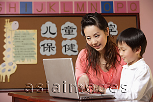 Asia Images Group - Teacher helping student use a laptop in class