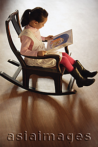 Asia Images Group - Girl sitting in rocking chair, reading a book