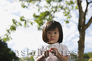 Asia Images Group - Young girl at park with flower, looking at camera