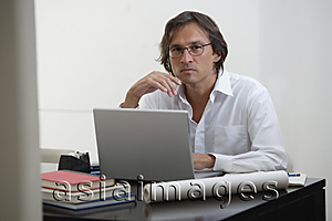 Asia Images Group - Businessman using laptop at the desk, looking at camera
