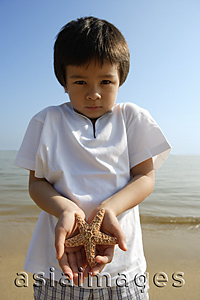 Asia Images Group - Young boy holding shell on both hands at the beach, looking at camera