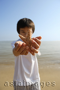 Asia Images Group - Young boy stretching out shell with both hands at the beach