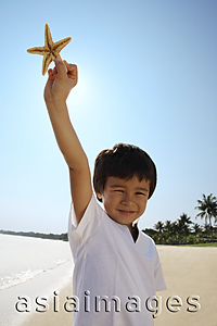 Asia Images Group - Young boy holding up shell at the beach, looking at camera