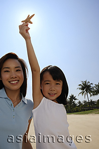 Asia Images Group - Mother with daughter holding up shell at the beach, smiling at camera