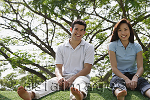 Asia Images Group - Young couple sitting on ground at the park, looking at camera