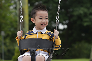 AsiaPix - Young boy on playground swing, smiling, looking away