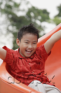 AsiaPix - Boy coming down playground slide, arms outstretched, smiling