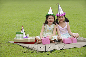 AsiaPix - Two girls wearing party hats sitting on picnic blanket, surrounded by gifts