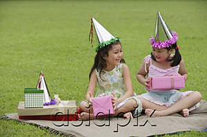 AsiaPix - Two girls wearing party hats sitting on picnic blanket, holding pink gift boxes