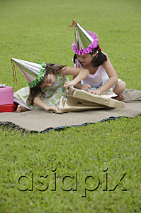 AsiaPix - Two girls wearing party hats sitting on picnic blanket, opening a gift
