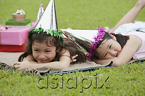 AsiaPix - Two girls wearing party hats lying on picnic blanket, resting