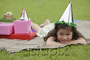AsiaPix - Girl lying on picnic blanket, wearing party hat, smiling at camera