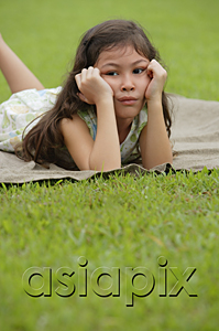 AsiaPix - Girl lying on picnic blanket, hands on face, sad expression