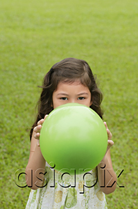 AsiaPix - Girl standing on grass, holding green balloon over her face