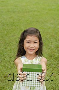 AsiaPix - Girl standing on grass, holding gift box towards camera