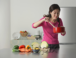 AsiaPix - Mature woman cooking in kitchen, looking at contents of pot