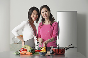 AsiaPix - Mother and adult daughter in kitchen preparing a meal, looking at camera