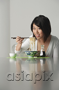 AsiaPix - Young woman sitting and eating a bowl of noodles
