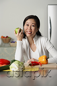 AsiaPix - Woman in kitchen, holding an apple, vegetables on table around her