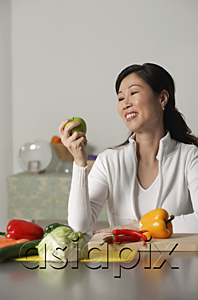 AsiaPix - Woman in kitchen, looking at apple, vegetables on table around her