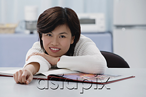 AsiaPix - Woman leaning on table, book open in front of her, smiling at camera