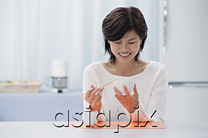AsiaPix - Woman in kitchen, holding bowl and chopsticks, eating