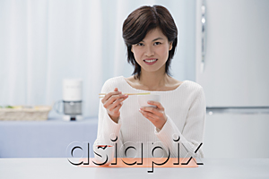 AsiaPix - Woman in kitchen, eating with chopsticks, looking at camera
