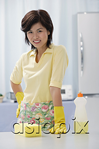 AsiaPix - Woman in kitchen, wearing gloves, looking at camera, cleaning detergent and sponge on kitchen counter
