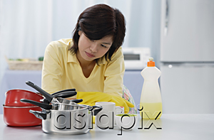 AsiaPix - Woman in kitchen, leaning on kitchen counter, looking at stack of pots and pans