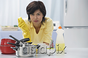 AsiaPix - Woman leaning on kitchen counter, holding cleaning sponge, stack of pots and pans in front of her