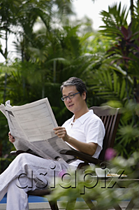 AsiaPix - Mature man sitting in garden, reading newspaper