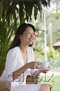 AsiaPix - Woman sitting on patio, holding cup and saucer