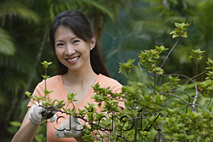AsiaPix - Woman in garden, pruning plants, smiling at camera