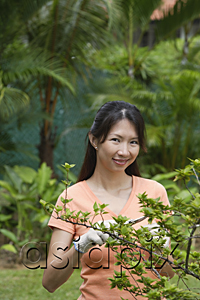 AsiaPix - Woman in garden, pruning plant, smiling at camera