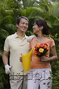 AsiaPix - Couple in garden, woman holding bouquet of flowers and watering can, smiling at man next to her