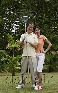 AsiaPix - Couple standing side by side in garden, man holding garden rake