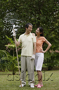 AsiaPix - Couple standing side by side in garden, looking at each other, man holding garden rake