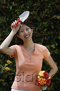 AsiaPix - Woman holding trowel and bouquet of flowers, wiping her brow