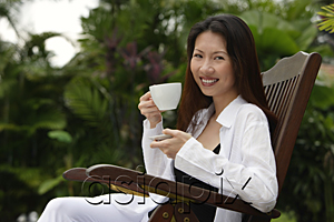 AsiaPix - Woman sitting outdoors, having a cup of tea, smiling at camera