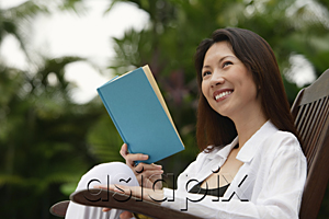 AsiaPix - Woman sitting outdoors, reading a book, looking away