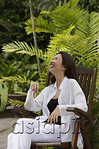 AsiaPix - Woman sitting in garden, smiling, looking up