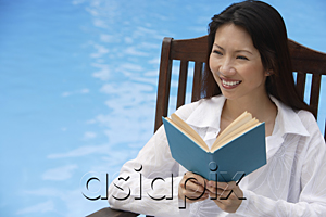 AsiaPix - Woman by swimming pool, reading a book, looking away